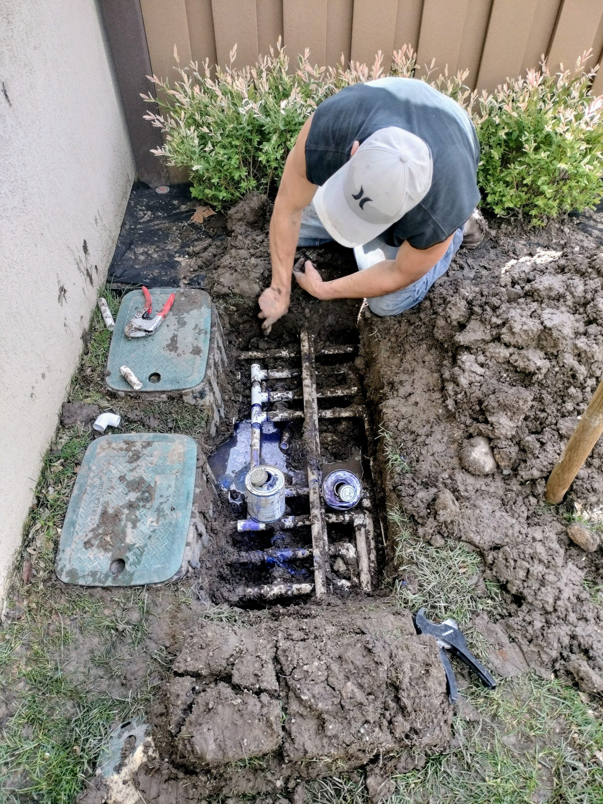 Technician working in a trench on irrigation pipes beside a building